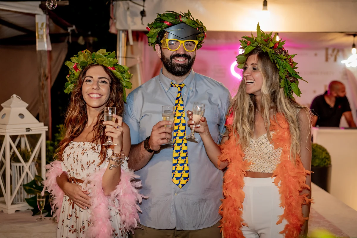Brindisi alla festa di laurea: tre invitati con la corona d'alloro e i calici alzati