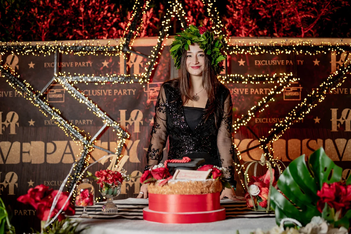 La neolaureata con la corona d'alloro dietro il tavolo della torta di laurea